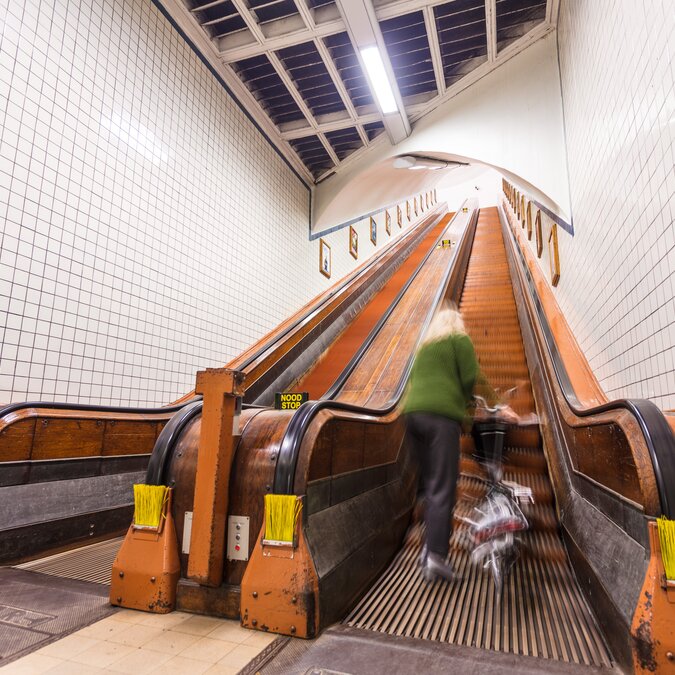Historische Holzrolltreppen im Sint‑Annatunnel in Antwerpen mit Person und Fahrrad. | © Piet de Kersgieter – Antwerpen Sint Annatunnel