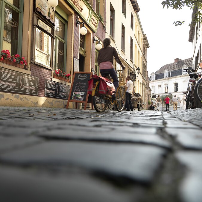 Cobbled street in Patershol, Ghent, with classic restaurants, bicycles, and historic facades. | © Milo Profi – Patershol, Ghent