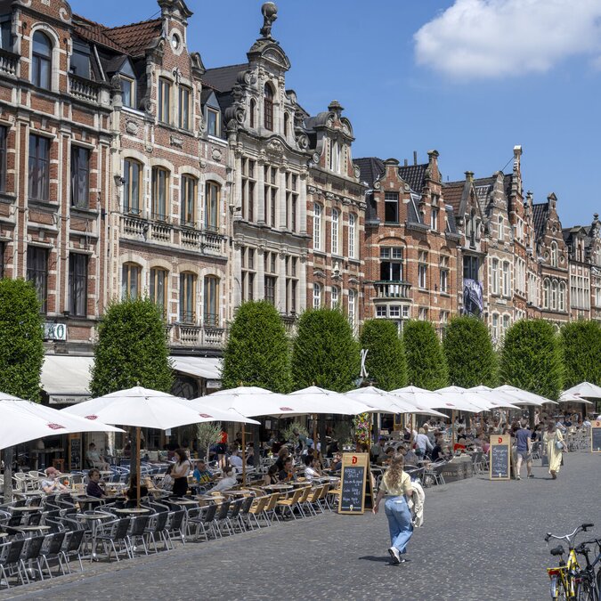 Belebter Platz in Leuven mit historischen Backsteinfassaden, gepflegten Baumreihen und zahlreichen Café‑Terrassen mit Sonnenschirmen. | © Karl Bruninx