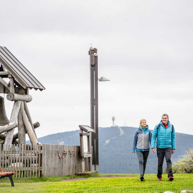 Zwei Personen wandern neben einer grossen Holzglocke im Erzgebirge | © TMGS Dennis Stratmann