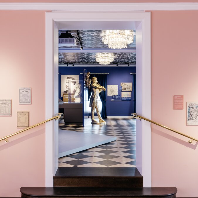 Vue à travers une entrée rose donnant sur une salle d'exposition présentant des sculptures et des objets historiques. | © Wien Tourismus |Gregor Hofbauer