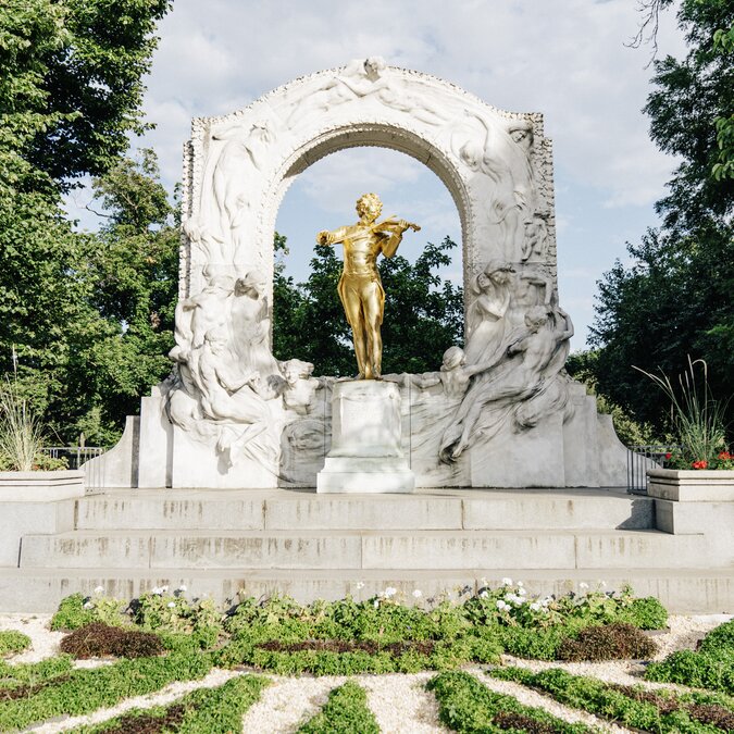 La statue dorée de Johann Strauss II se dresse dans le Stadtpark de Vienne, sous une arche en marbre blanc richement décorée. | © Wien Tourismus | Gregor Hofbauer